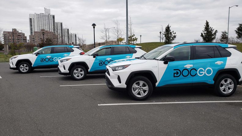 Three blue-and-white cars branded with DocGo's company logo.